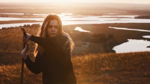 Young woman in black clothes training with a sword while early sunset on nature — Stock Video