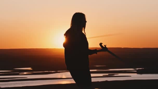 Młoda kobieta w czarnych ubraniach trening z dwoma mieczami podczas zachodu słońca na łonie natury — Wideo stockowe