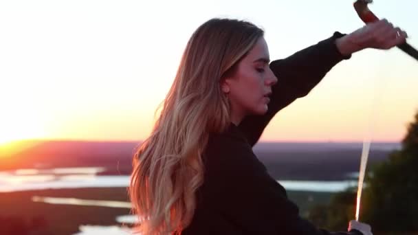 Svärd utbildning - ung vacker kvinna med blont hår utbildning med två svärd på bakgrunden av solnedgången — Stockvideo