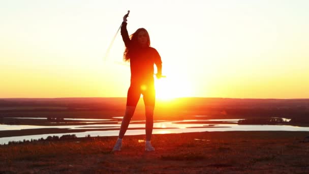 Zwaarden training - jonge vrouw met lang haar training met twee zwaarden op de achtergrond van de heldere zonsondergang — Stockvideo