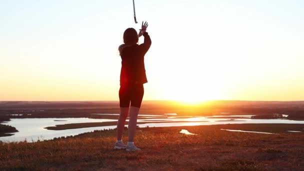 Zwaarden training - jonge vrouw met lang haar zwaaien met een zwaard op de achtergrond van de heldere zonsondergang — Stockvideo