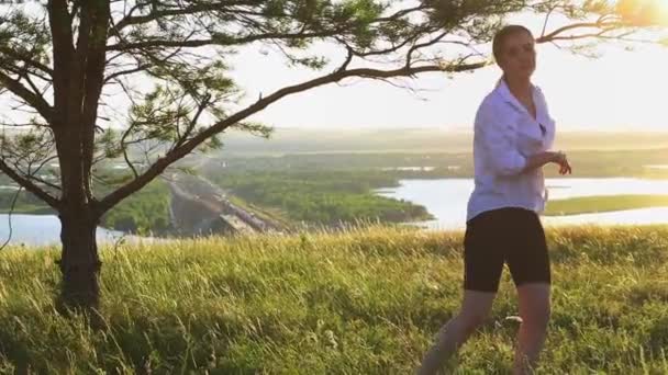 Svärd träning - ung vacker kvinna i vit skjorta viftar med ett svärd på naturen tidigt på kvällen - tittar i kameran — Stockvideo