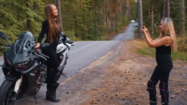 Mujeres sonrientes amigas sentadas en motocicletas en el bosque y tomando fotos por teléfono — Vídeos de Stock