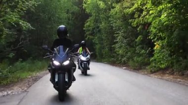 Ormanda motorsikletler. Dar yolda motosiklet süren iki kadın.