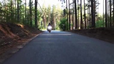 Ormandaki boş dar yolda motosiklet süren iki kadın.