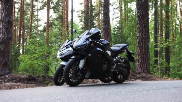 Két fekete motorkerékpár áll az út szélén az erdőben. — Stock videók