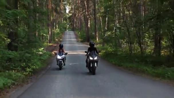 Dos mujeres montando motocicletas en una carretera vacía y estrecha en el bosque a la luz del día — Vídeo de stock