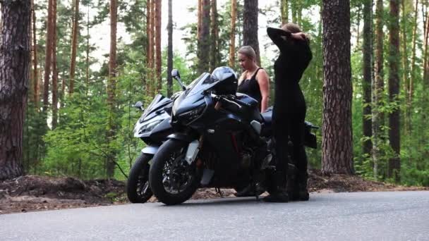 Moto nella foresta - due donne adulte camminano verso le loro moto sulla strada stretta e vuota e si preparano per il viaggio — Video Stock