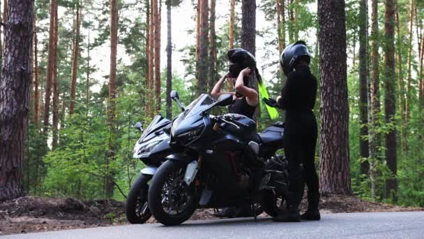 Motorräder im Wald - zwei erwachsene Frauen bereiten sich auf die Fahrt auf Motorrädern vor - setzen Helme auf — Stockvideo