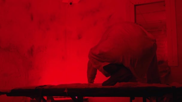 Szalony człowiek w kaftanie bezpieczeństwa czołgający się po stole w szpitalu psychiatrycznym — Wideo stockowe