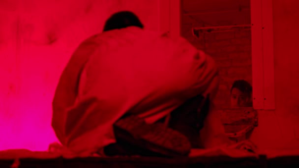 Szalony mężczyzna w kaftanie bezpieczeństwa siedzi na łóżku w szpitalu psychiatrycznym, trzęsąc się i patrząc w lustro — Wideo stockowe