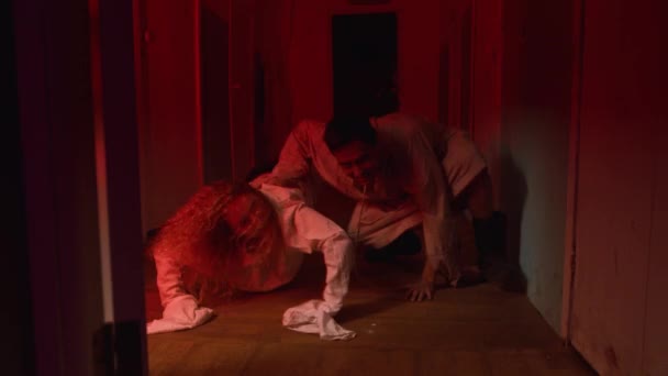 Skräckskådespeleri - man och kvinna kryper i korridoren av skrämmande blodiga mentalsjukhus till kameran — Stockvideo