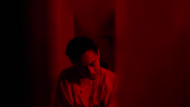 Uomo pazzo in camicia di forza che cerca di togliersi i vestiti nella cella dell'ospedale psichiatrico con l'illuminazione rossa — Video Stock