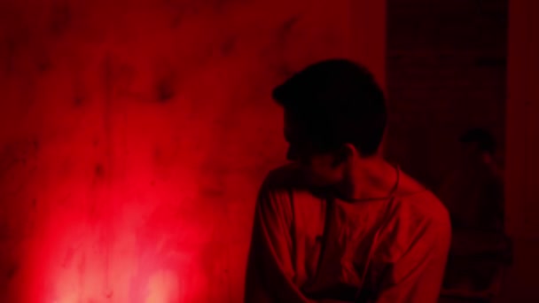 Безумный человек в смирительной рубашке дергается и пытается вылезти из одежды в камере психбольницы при красном освещении — стоковое видео
