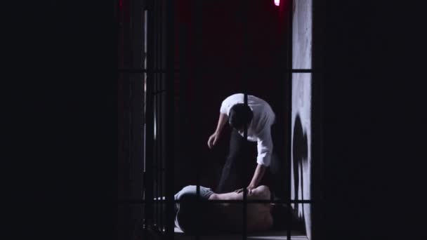 Действие ужаса - надзиратель избивает заключенного, лежащего на земле в тюрьме — стоковое видео