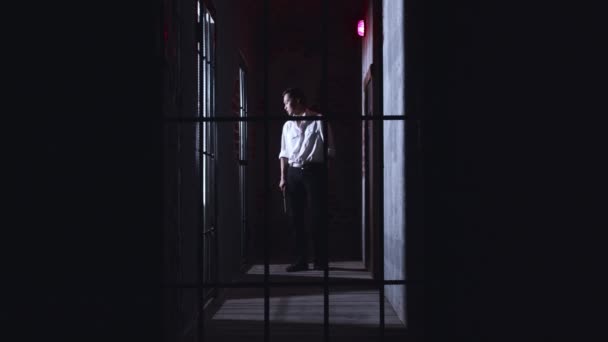 Horror acting - un pericoloso guardiano maschio fa un giro delle celle della prigione con un tubo metallico e urla ai prigionieri dietro le sbarre — Video Stock