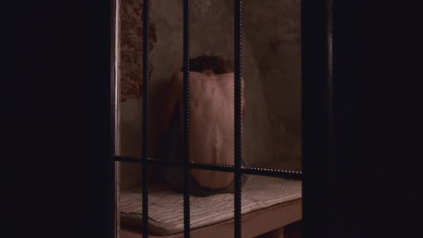 Horror acting - a shirtless man struggling sitting on the bed in the prison cell — Stock Video