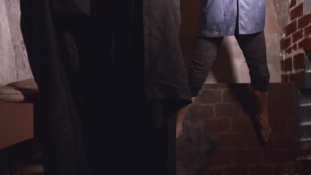 Horror színészkedés - egy férfi egy zacskóval a fején felakasztották a plafonra, és a hóhér felolvas egy imát — Stock videók