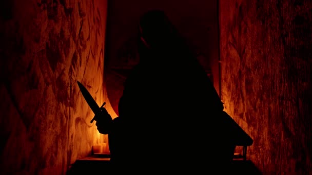 En man ockultist i svarta kläder står med en kniv i händerna — Stockvideo