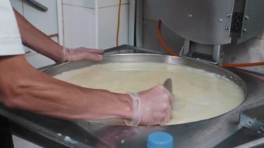 Peynir üretimi - erkek işçi fıçıda taze peyniri büyük bir demir tabakla karıştırıyor.