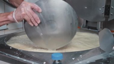 Peynir endüstrisi - eldivenli erkek işçi fıçıda yumuşak peyniri büyük bir demir tabakla karıştırıyor.