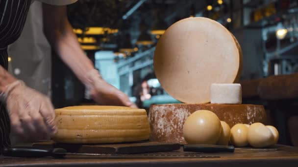 Un hombre en una tienda de quesos corta una enorme cabeza de queso por la mitad. — Vídeo de stock