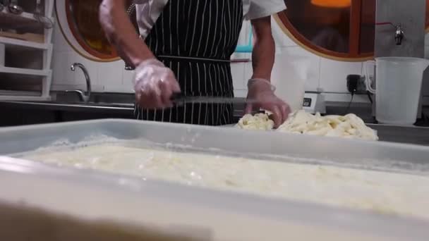 Un operaio in guanti che taglia strisce di formaggio e lo mette nella vasca con del liquido — Video Stock