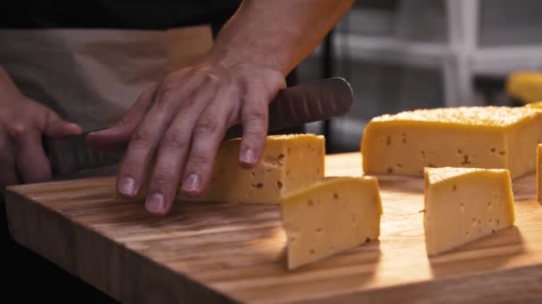 En man skär ett stort huvud ost i bitar för servering — Stockvideo