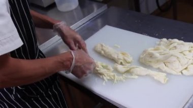 Peynir üreten fabrika. Eldiven giyen işçi peyniri parçalara ayırıyor.