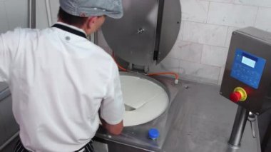 Eldivenli bir adam fıçıda taze peyniri büyük bir kesici aletle karıştırıyor.