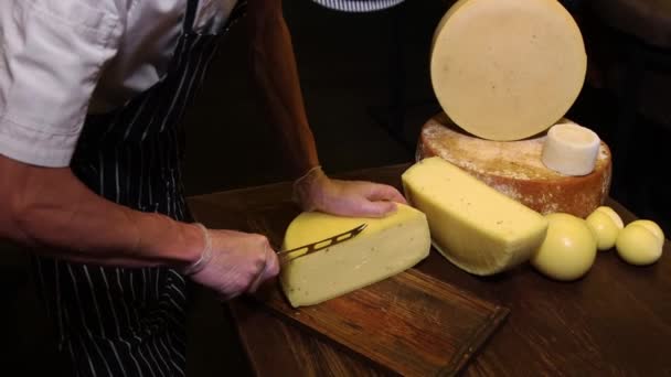 Service au restaurant - homme coupant un petit morceau d'une tête de fromage avec un couteau — Video