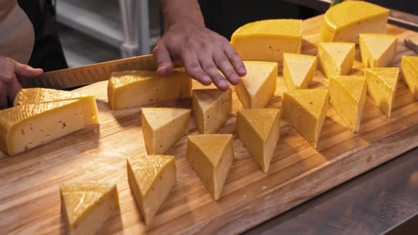 Um homem na loja corta uma cabeça de queijo com uma faca grande em pedaços triangulares semelhantes. — Vídeo de Stock