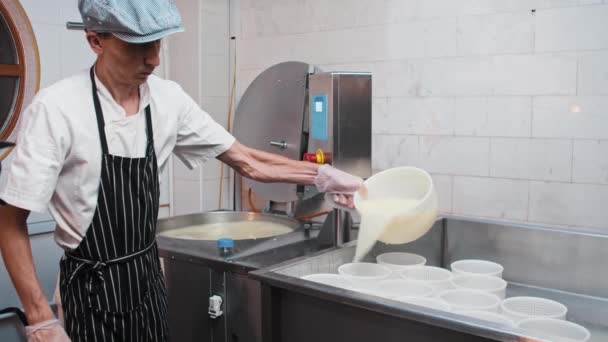 La fábrica de quesos - hombre con guantes que trabaja con una máquina para hacer queso - filtra el líquido con queso blando a través de un colador — Vídeos de Stock