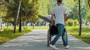 Bir adam yaz parkında tekerlekli sandalyede bir kadınla oynuyor.