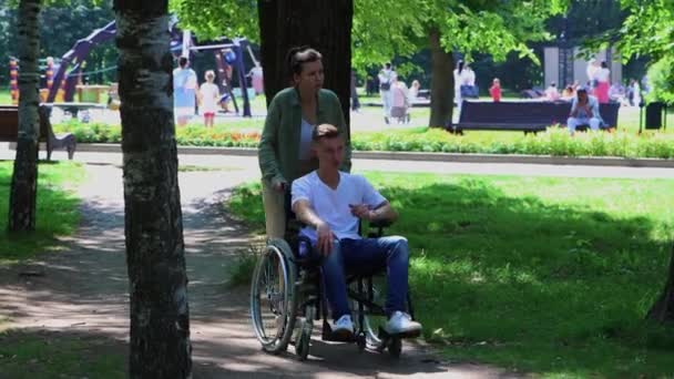 Una mujer caminando con un tipo en silla de ruedas en el parque — Vídeos de Stock