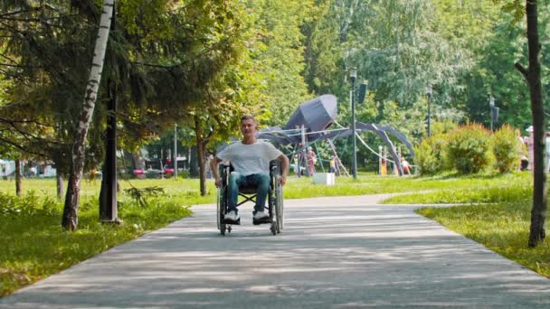 En kille i rullstol åker i parken på sommaren — Stockvideo