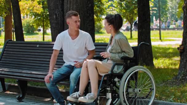 Egy pár a parkban - egy srác beszél fogyatékkal élő nővel egy padon — Stock videók