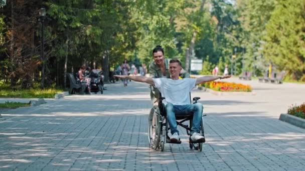 Amigos caminando en el parque - un hombre en silla de ruedas y su amiga haciendo el tonto — Vídeo de stock