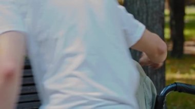 Bir adam tekerlekli sandalyedeki kadına eşlik ediyor ve ayağa kalkmasına yardım ediyor.