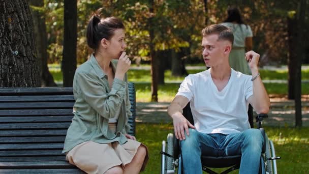 Teman-teman berjalan di taman - seorang pria di kursi roda dan teman wanitanya duduk dan melihat orang lain — Stok Video