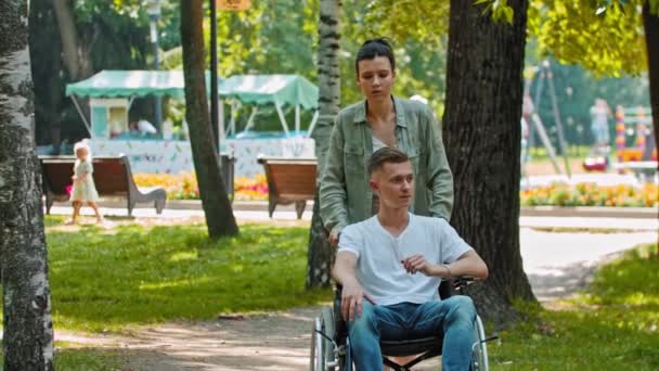 Amigos caminhando no parque - um homem em uma cadeira de rodas e sua amiga indo na parte deserta do parque e conversando — Vídeo de Stock