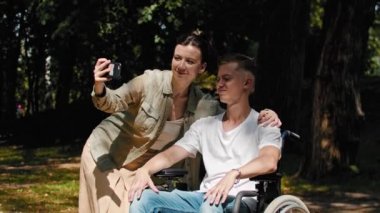 Tekerlekli sandalyedeki bir adam ve kız arkadaşı yaz parkında vakit geçiriyorlar ve birlikte selfie çekiyorlar.