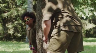 Küçük siyah kız ve annesi parkta oynuyorlar. Ağacın arkasından dışarı bak.