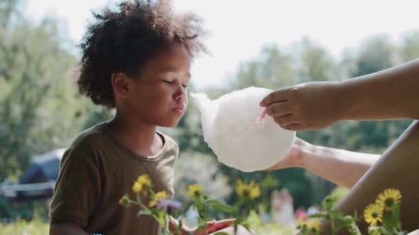 Black little girl eating cotton candy from her mothers hands outdoors — Stock Video
