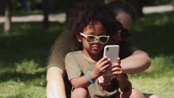 Μικτή οικογένεια μητέρας και κόρης που περνούν χρόνο στο πάρκο και παίζουν με το τηλέφωνο — Αρχείο Βίντεο