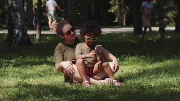 Famille mixte de mère et fille passant du temps dans le parc et la fille jouant à des jeux au téléphone — Video