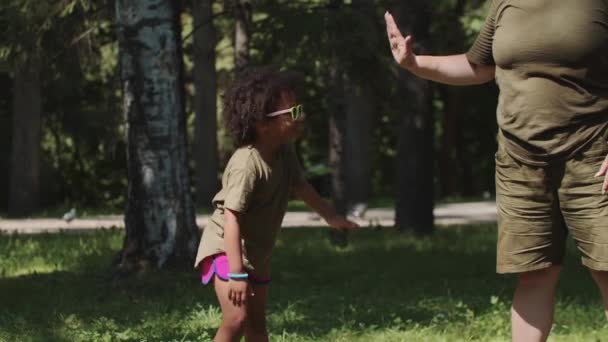 Vit kvinna och hennes svarta dotter ger varandra en high five i parken — Stockvideo