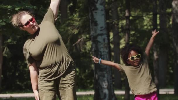 Blanke vrouw en haar zwarte dochtertje doen eenvoudige oefeningen in het park — Stockvideo