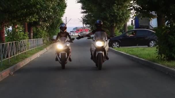 Dos mujeres jóvenes que conducen lentamente motocicletas en carretera estrecha y cogidas de la mano — Vídeo de stock