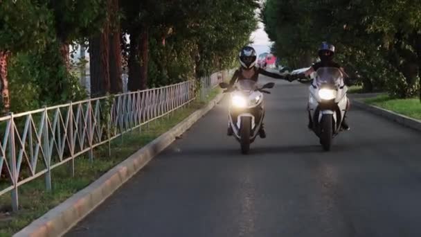 Dos jóvenes montan lentamente motocicletas en una carretera y se toman de la mano — Vídeos de Stock